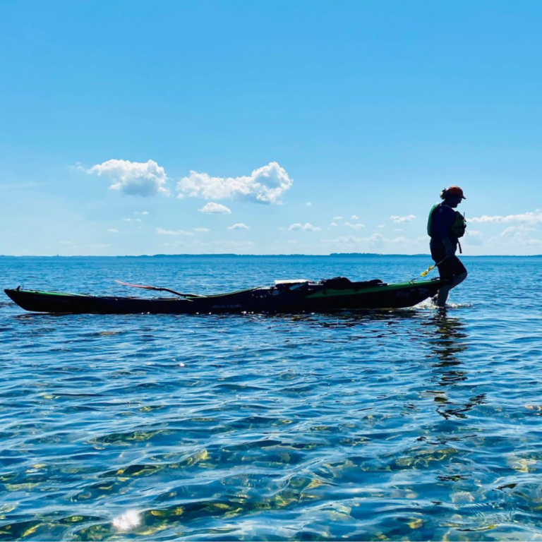 Person i kajak på lugnt vatten med blå himmel och några moln i bakgrunden.
