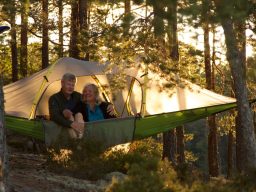 Ett par sitter i en hängmatta mellan träden, omgiven av naturen.