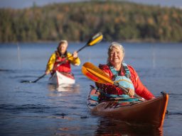 Två personer paddlar i kajak på Vättern omgiven av skog.