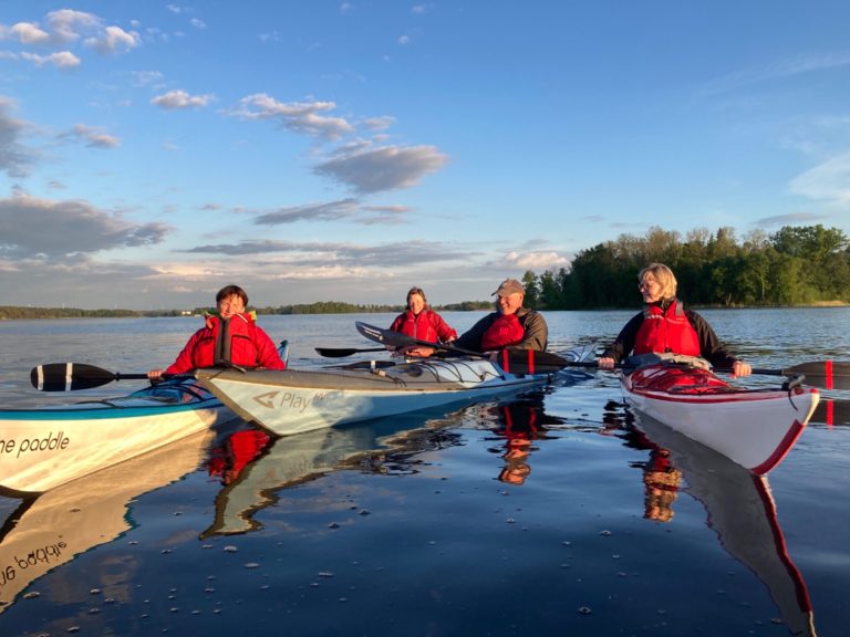 Fyra personer i kajaker på en stilla sjö under en solig himmel.