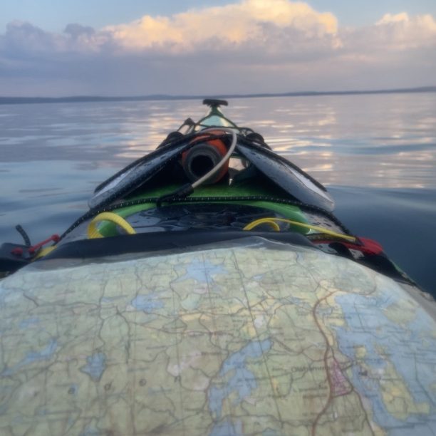 Karta på kajak, spegelblanka vatten och mjuka moln i bakgrunden.