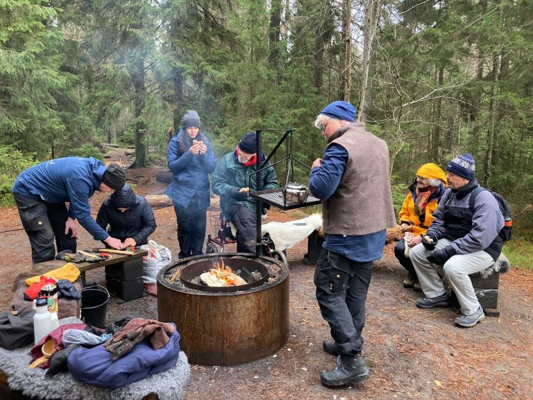 Grupp som lagar mat tillsammans vid en eld efter en guidad tur i Tiveden